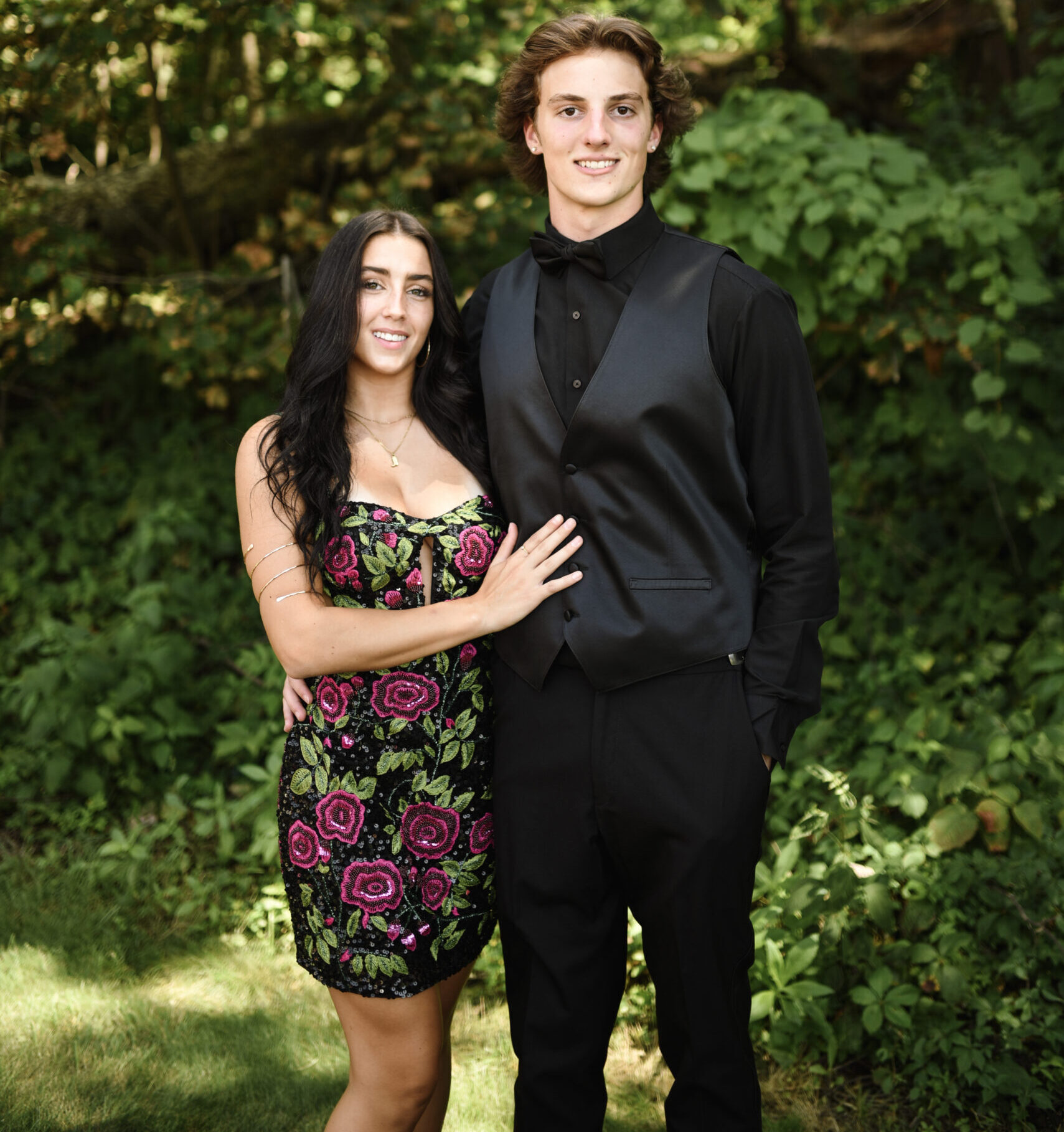 Young couple posing for their prom in a black suit with black shirt and black tie and a girl in a black dress with flowers on it!